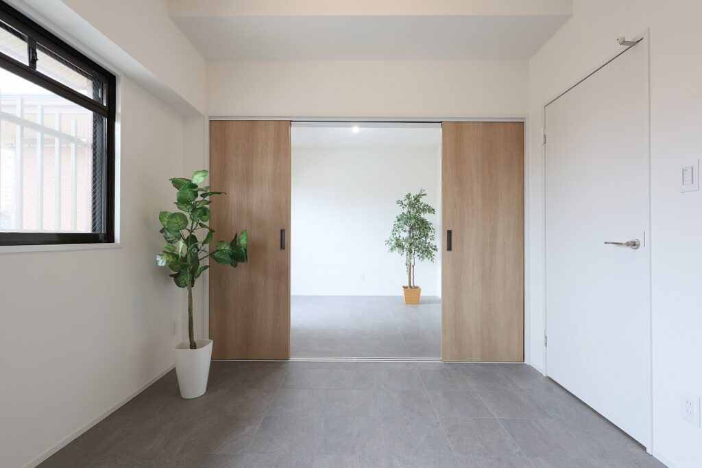 木目調の引き戸がやさしい印象を与える室内空間。床はグレー系のタイルで統一され、落ち着いたモダンな雰囲気を演出しています。引き戸にはLIXILの「ラシッサ」を採用し、デザイン性と機能性を両立。観葉植物がアクセントとなり、シンプルで心地よい空間に仕上がっています。