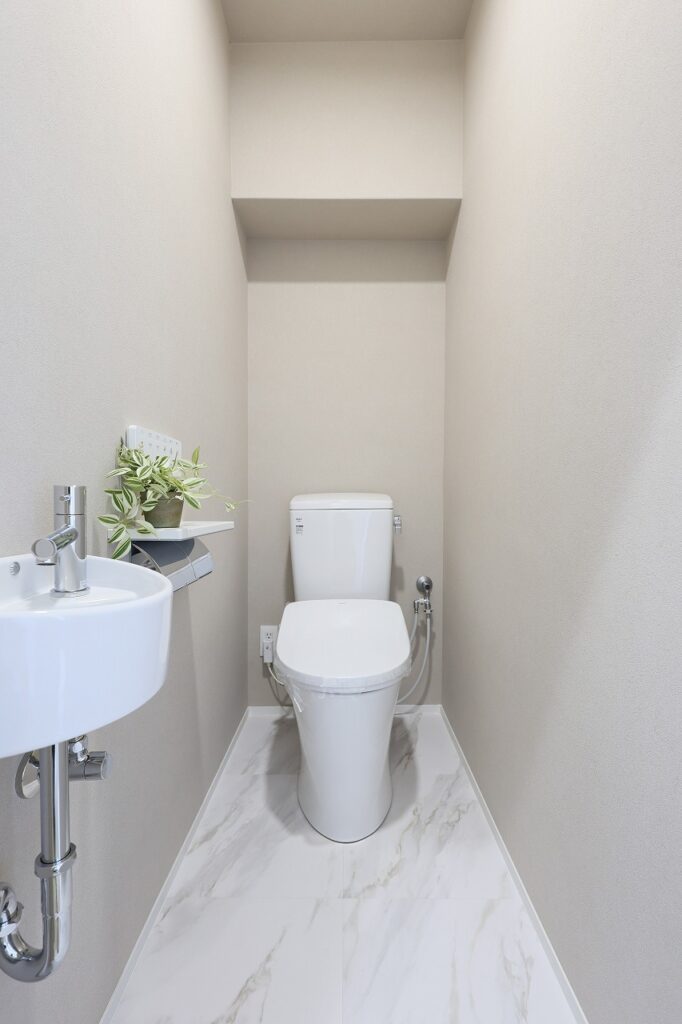 限られたスペースをすっきりとまとめたトイレ空間。清潔感のあるホワイトに大理石調の床材を合わせ、上品で明るい印象に仕上げました。手洗い器にはミラタップ製のコンパクト手洗い器を採用。シンプルで場所を取らず、狭小空間でも使いやすさとデザイン性を両立しています。小さなグリーンが空間にやさしい彩りを添えています。