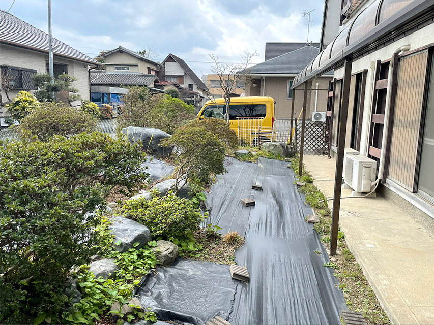 リノベーション前の庭の様子。防草シートと植栽が残る状態で、外壁や窓周りの古い設備も確認できる記録写真