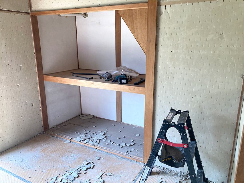 押し入れ周りの壁材を撤去した室内の様子。床には解体した破片が落ち、工具が並ぶ状態を記録した写真