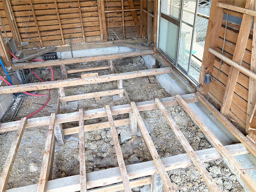 床材を撤去し、土台と大引きがむき出しになった室内の様子。リノベーションに向けて配管や基礎部分の確認が進んでいる状態を写した写真。