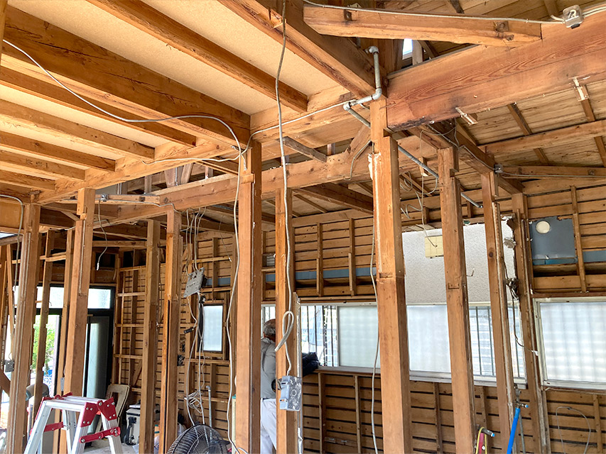 壁材を撤去して柱や梁が露わになった室内の様子。電気配線がむき出しになり、職人が内部構造を確認しながら作業を進めている状況を写した写真。