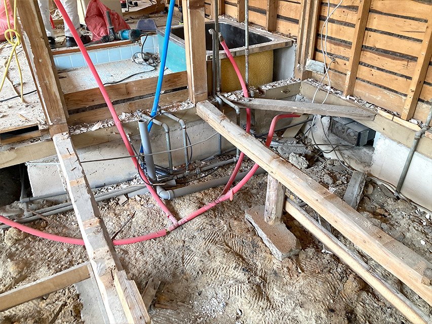 床下の給排水管が見える状態で、赤と青の配管が新旧混在しながら確認・整理されている様子。