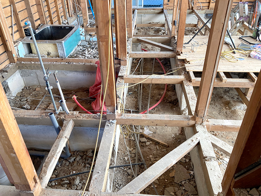 住宅の床を解体した段階で、土台や基礎、配管が露出した状態を写した写真。床下の構造がよく見える状況を説明したもの。