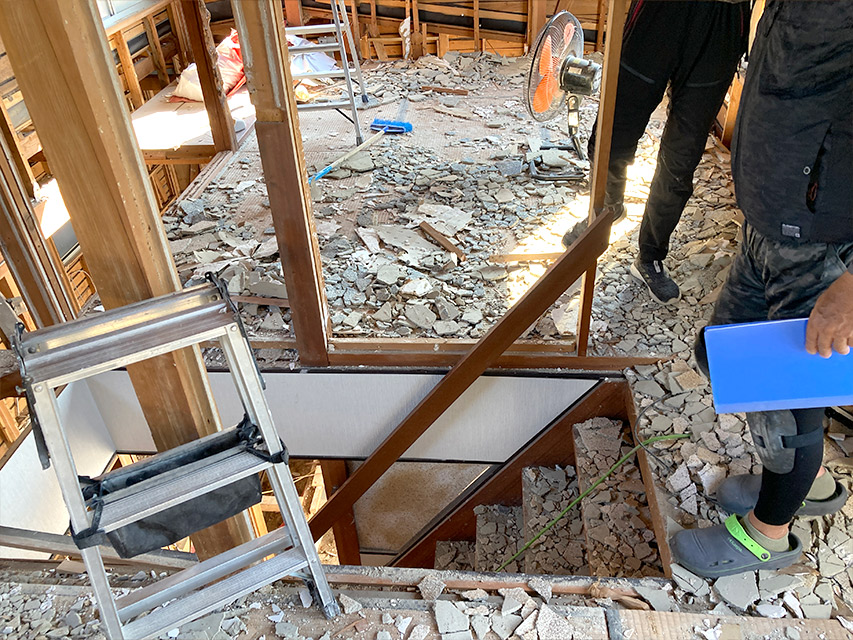 住宅の解体工事現場で、床材の破片が広がる室内と階段まわりの様子を撮影した写真。