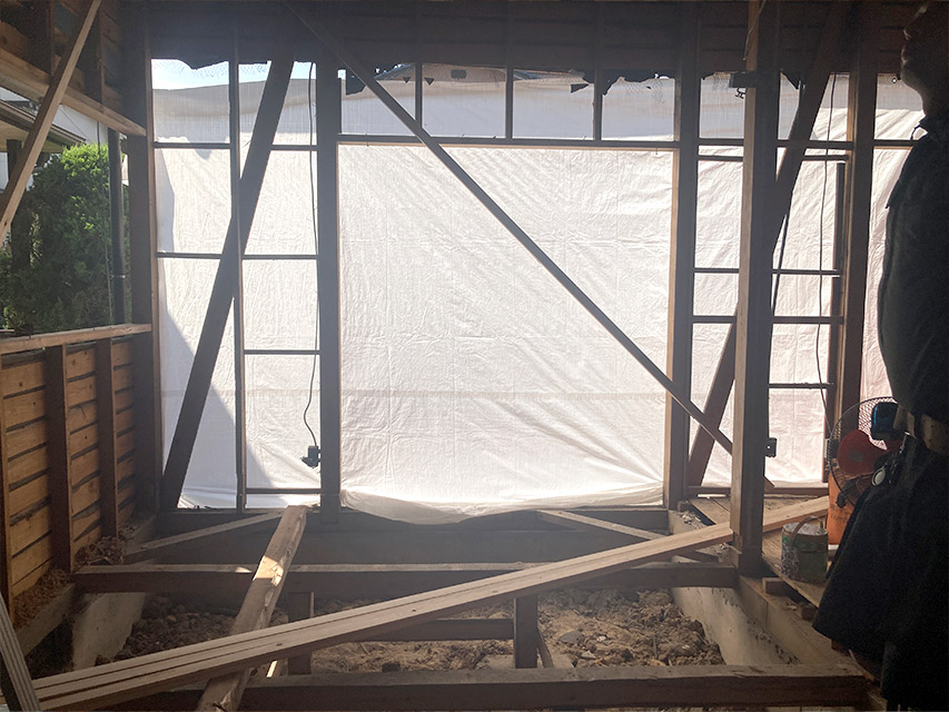 室内の壁が解体され、骨組みだけになった状態を写した写真で、外側には養生シートが張られ光が透ける様子が見えている状況を説明しています。