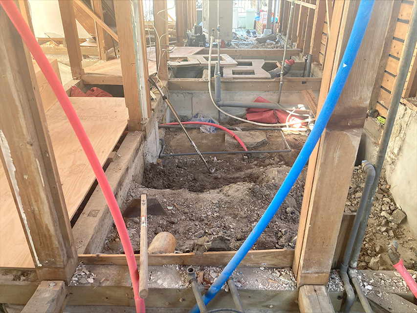 床下部分が大きく掘り下げられ、給排水管や配線が見えている室内の解体途中の様子を写した写真
