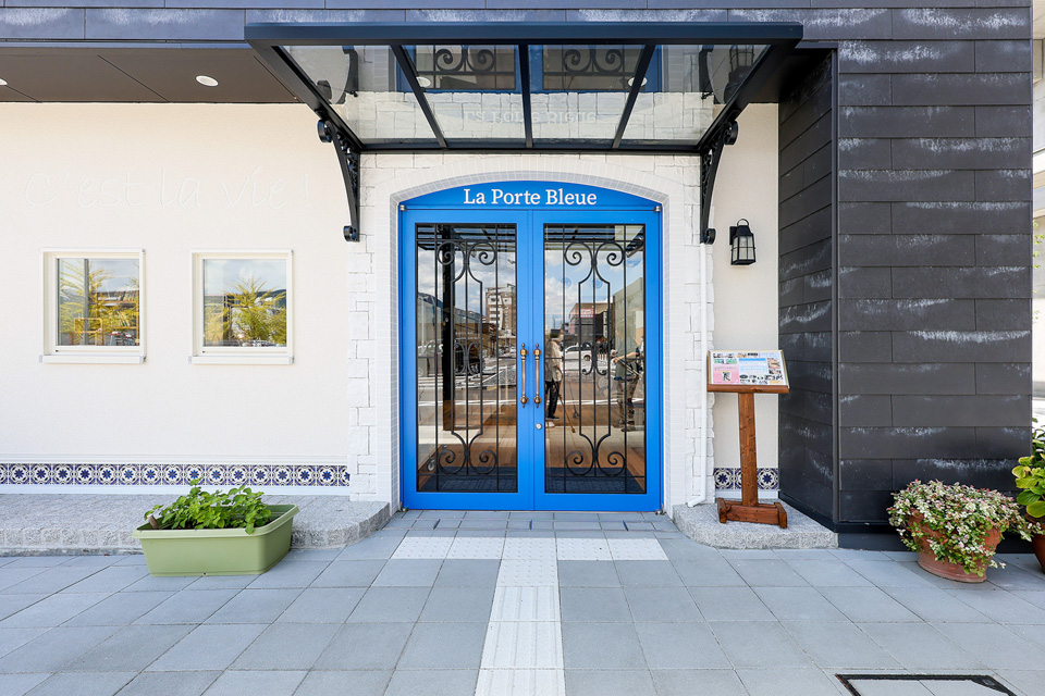 青い扉、石積みの玄関、ロートアイアンのキャノピー（庇） 壁はフランス生まれの塗材をコテで仕上げました。