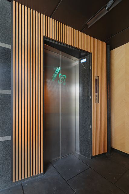 エレベーターホールは不燃木を使用し、温かみのある空間に仕上ました。 扉にはプロジェクターで社名ロゴサインを投影しています。