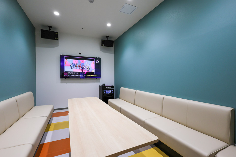 大人数用のカラオケルームはカリフォルニアブルーの壁紙と海辺の太陽やサンセットを彷彿させる暖色系床材で西海岸風の空間へ仕上げました。