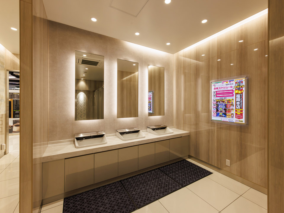 トイレ内洗面カウンターです。天板は人造大理石で、全自動手洗器をすっきり納めています。鏡背面にも間接照明を用い、落ち着いた雰囲気を醸し出しています。